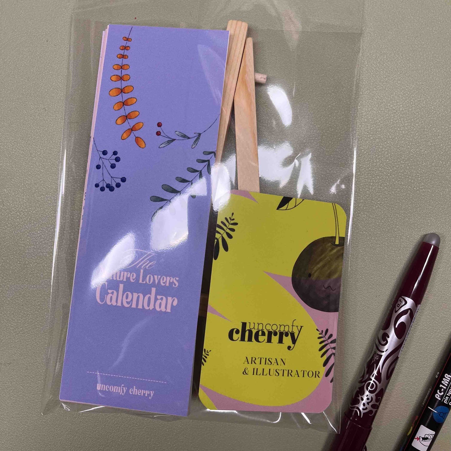 Colorful Uncomfy Cherry calendar with whimsical monthly designs, standing on a small easel.