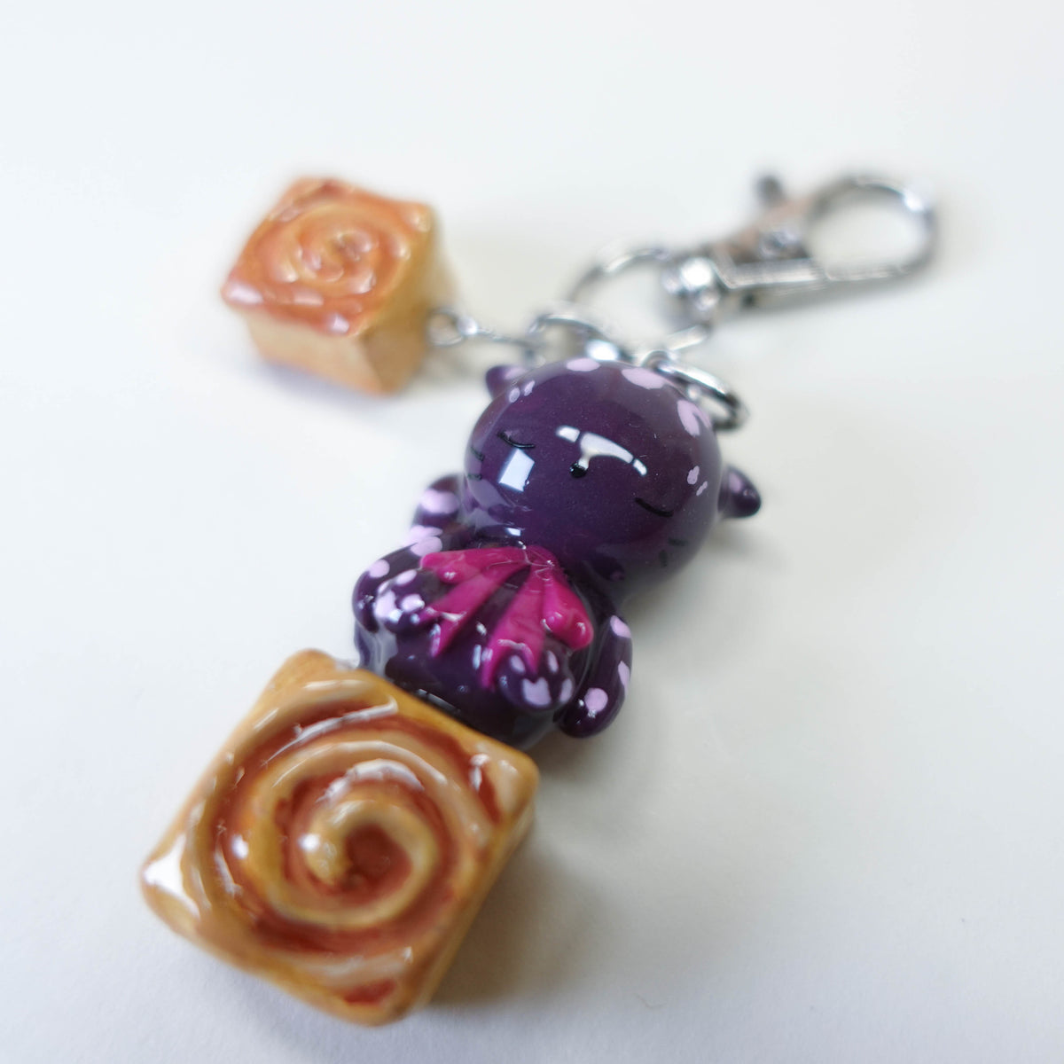 Cinna Cat sitting on a cinnamon bun, cute kawaii handmade polymer clay keychain by Uncomfy Cherry, part of the Midnight Picnic collection in brown