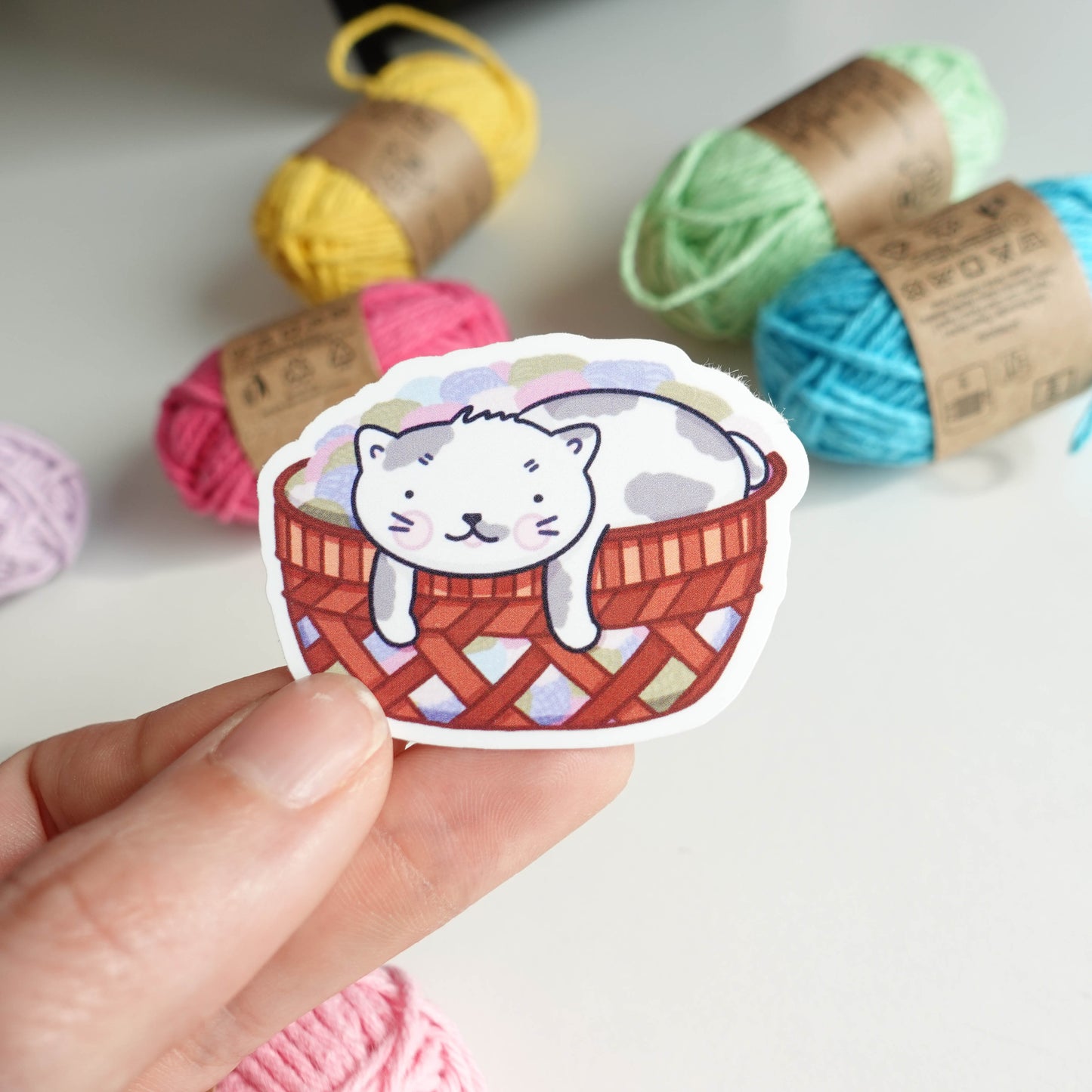 Yarn Basket Cat Sticker featuring an adorable cat nestled in a yarn basket design, perfect for adding charm to laptops, notebooks, and water bottles.