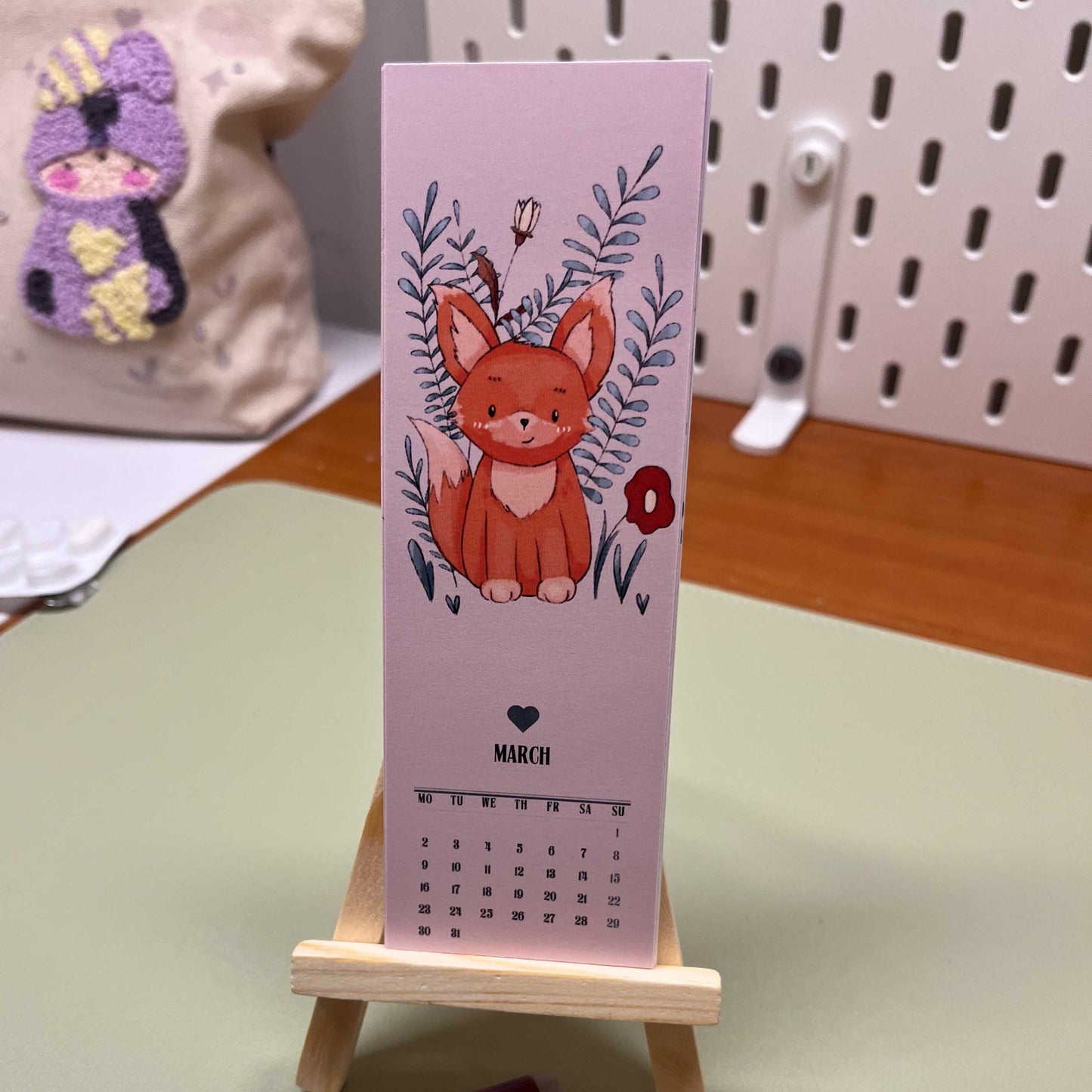 Adorable illustrated calendar featuring Uncomfy Cherry characters, shown with a tiny easel for display.