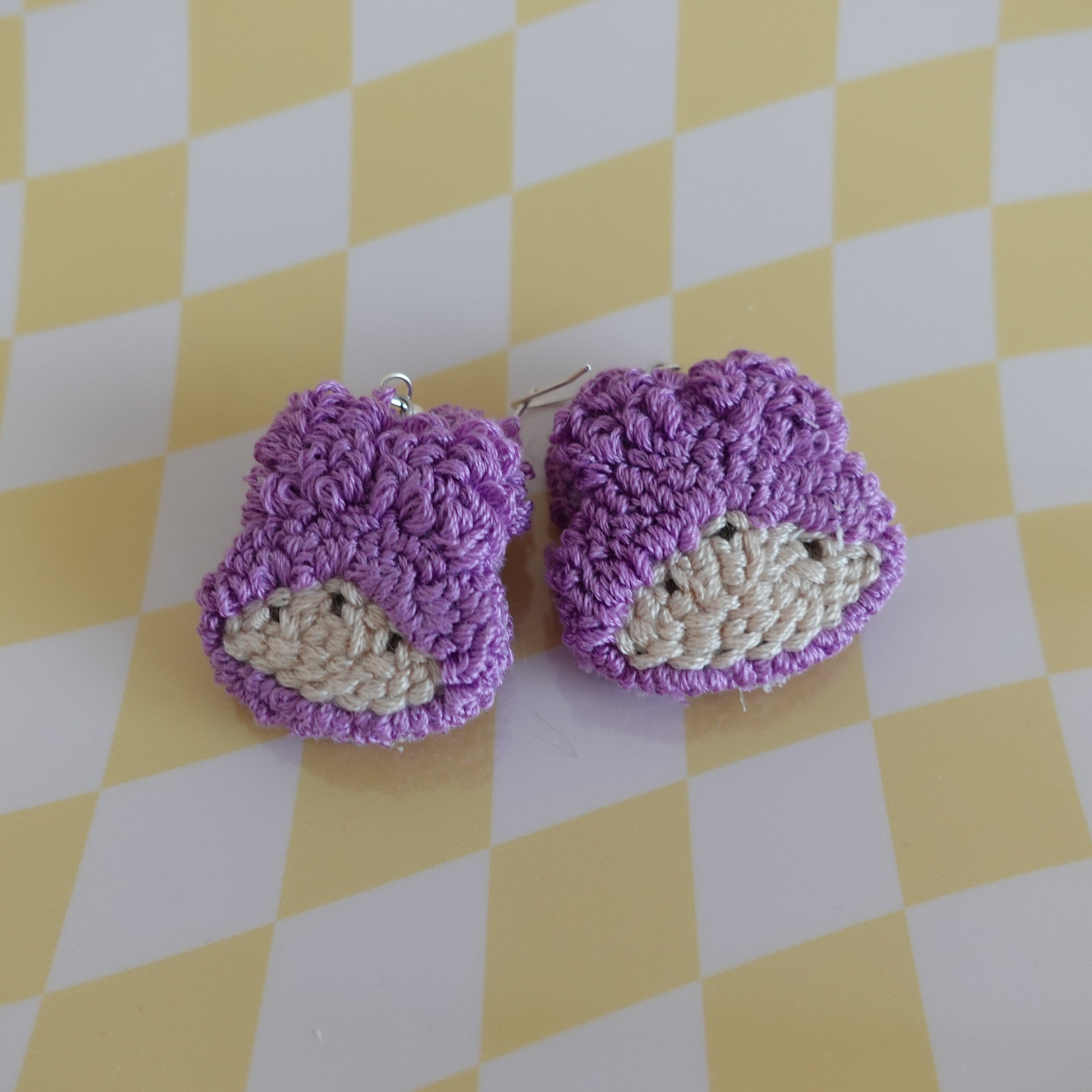 Close-up of a handmade punch needle earring in purple featuring intricate textile work.