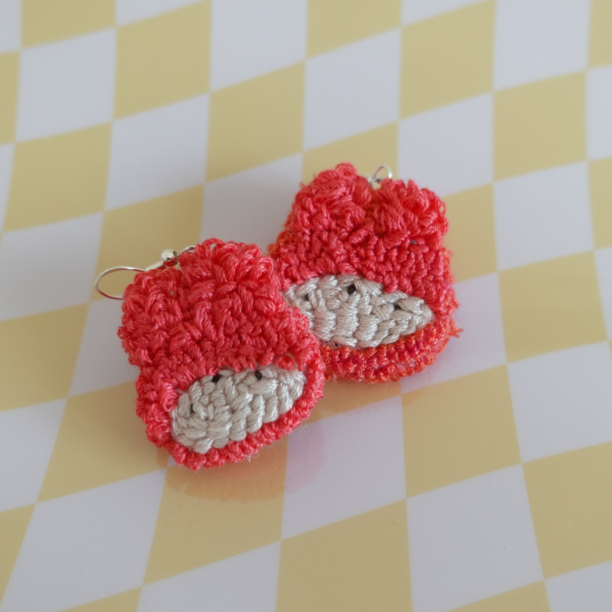 Close-up of a handmade punch needle earring in red featuring intricate textile work.