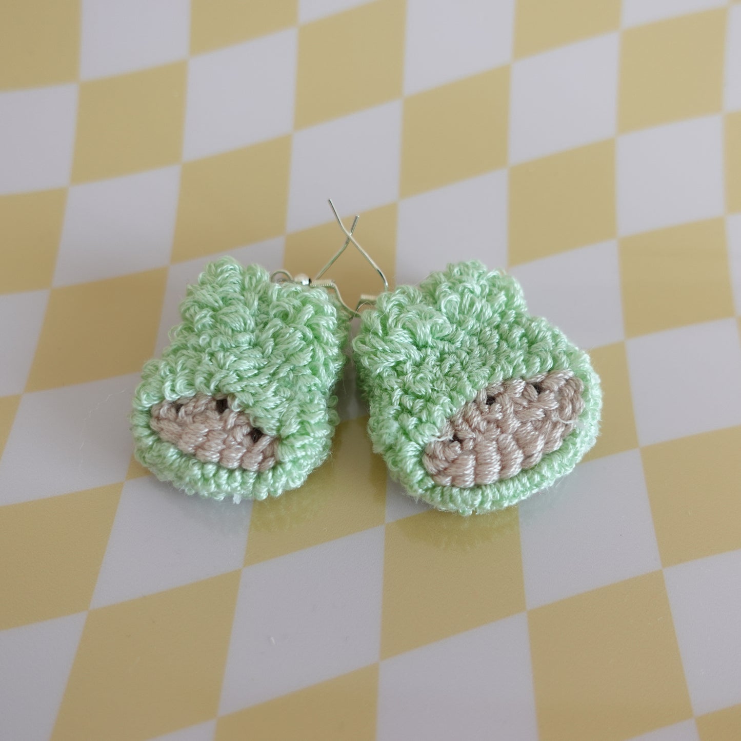 Close-up of a handmade punch needle earring in teal featuring intricate textile work.