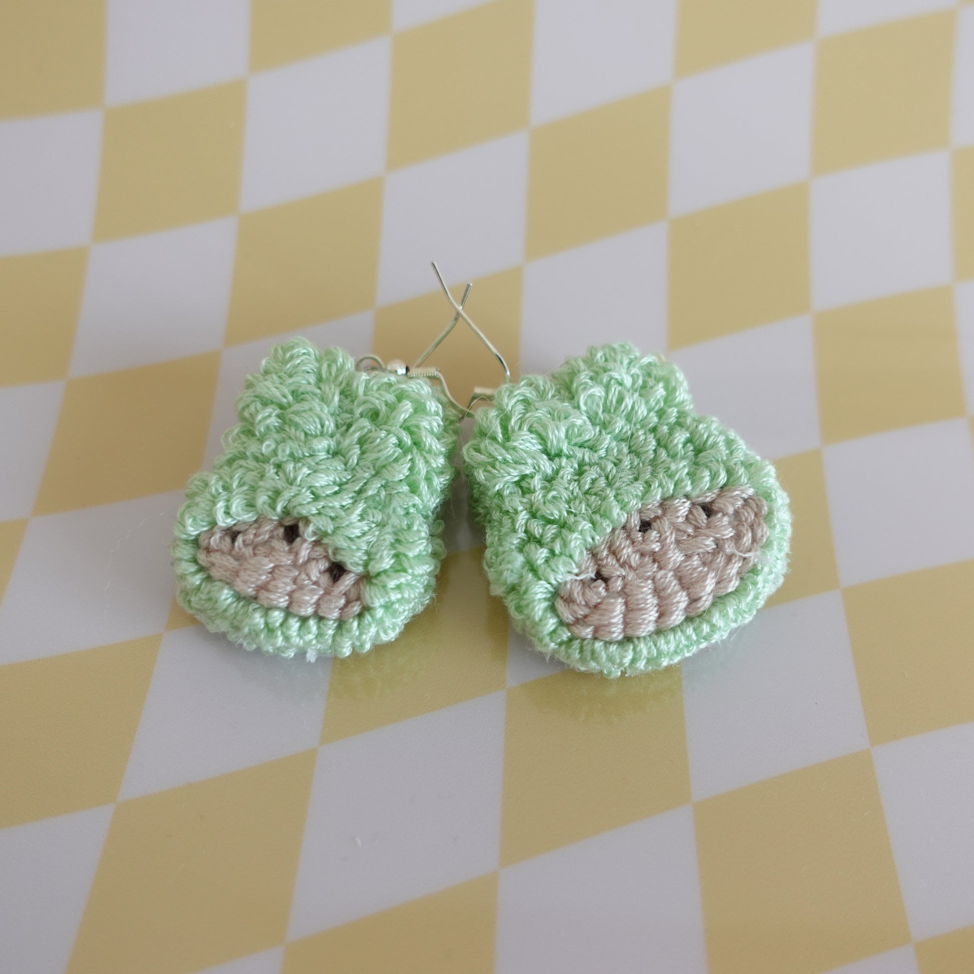 Close-up of a handmade punch needle earring in teal featuring intricate textile work.