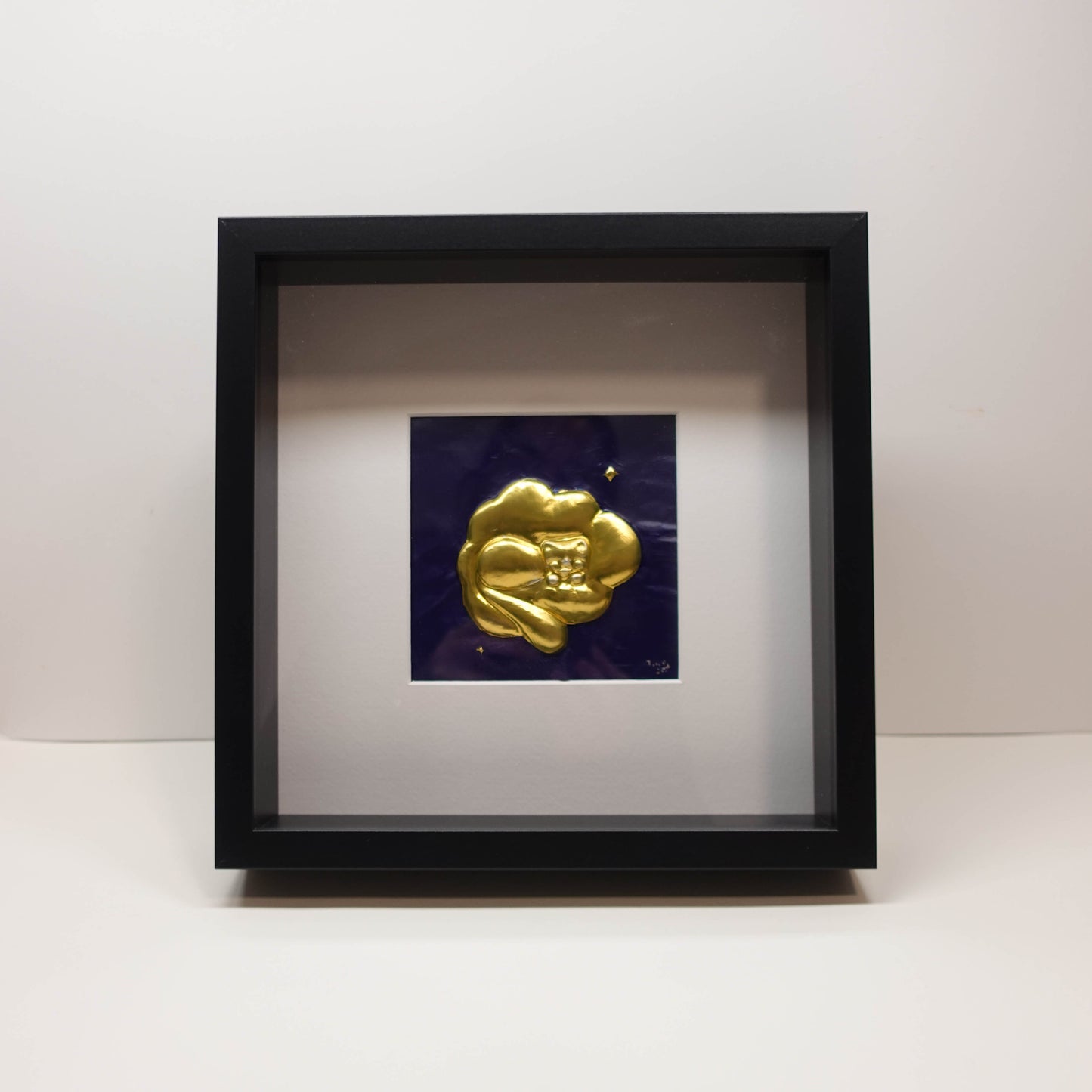 Brass 3D sculpture of a sleeping cat resting on clouds, set against a painted blue background in a recessed frame, 25 × 25 cm.