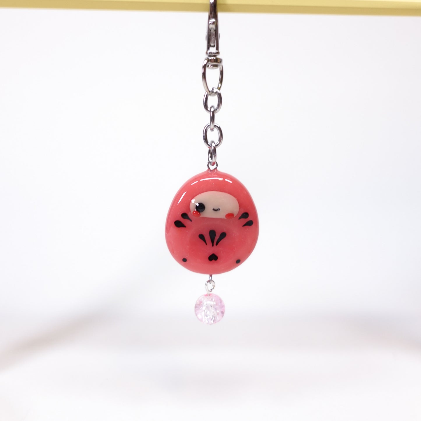 Uncomfy Cherry Daruma worry stone keychain clipped to bag