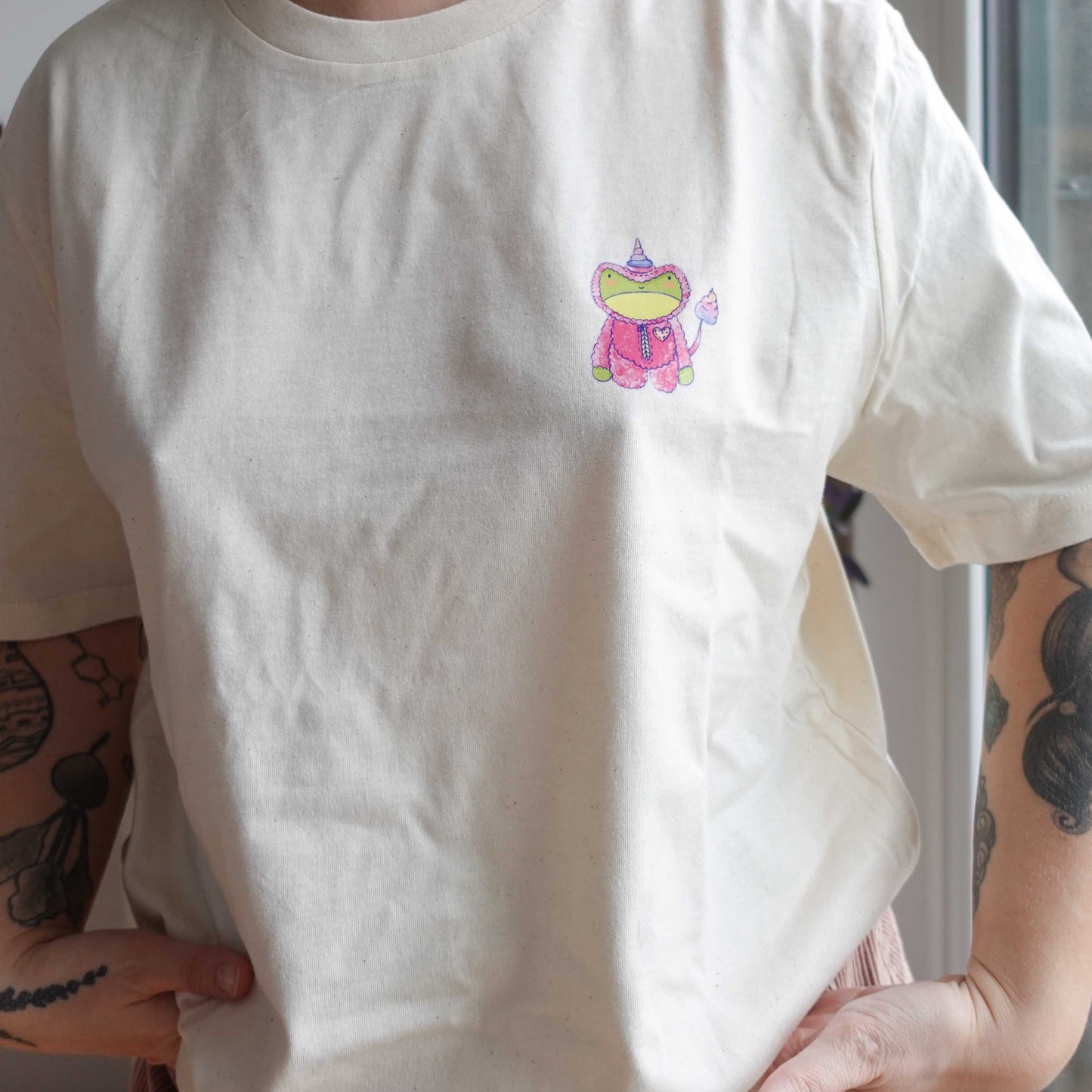 Front view of the Fluff Club  t-shirt in natural raw color, featuring a original design by uncomfy cherry from the frog in a unicorn suit