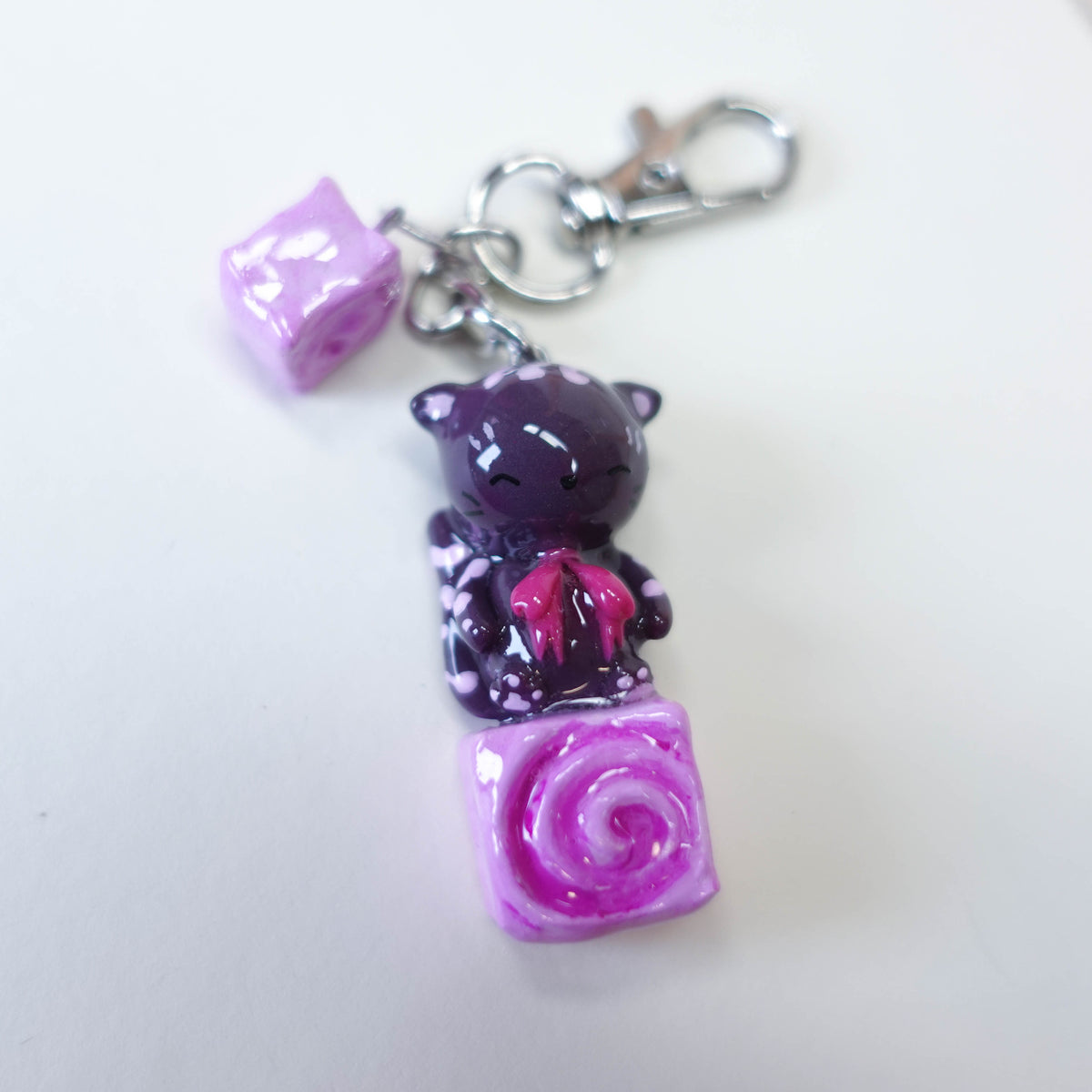 Cinna Cat sitting on a cinnamon bun, cute kawaii handmade polymer clay keychain by Uncomfy Cherry, part of the Midnight Picnic collection in pink