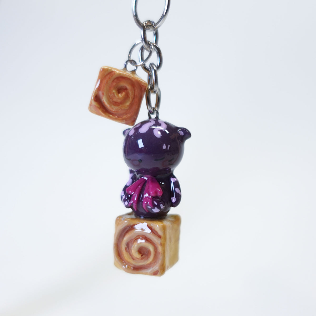 Cinna Cat sitting on a cinnamon bun, cute kawaii handmade polymer clay keychain by Uncomfy Cherry, part of the Midnight Picnic collection in brown