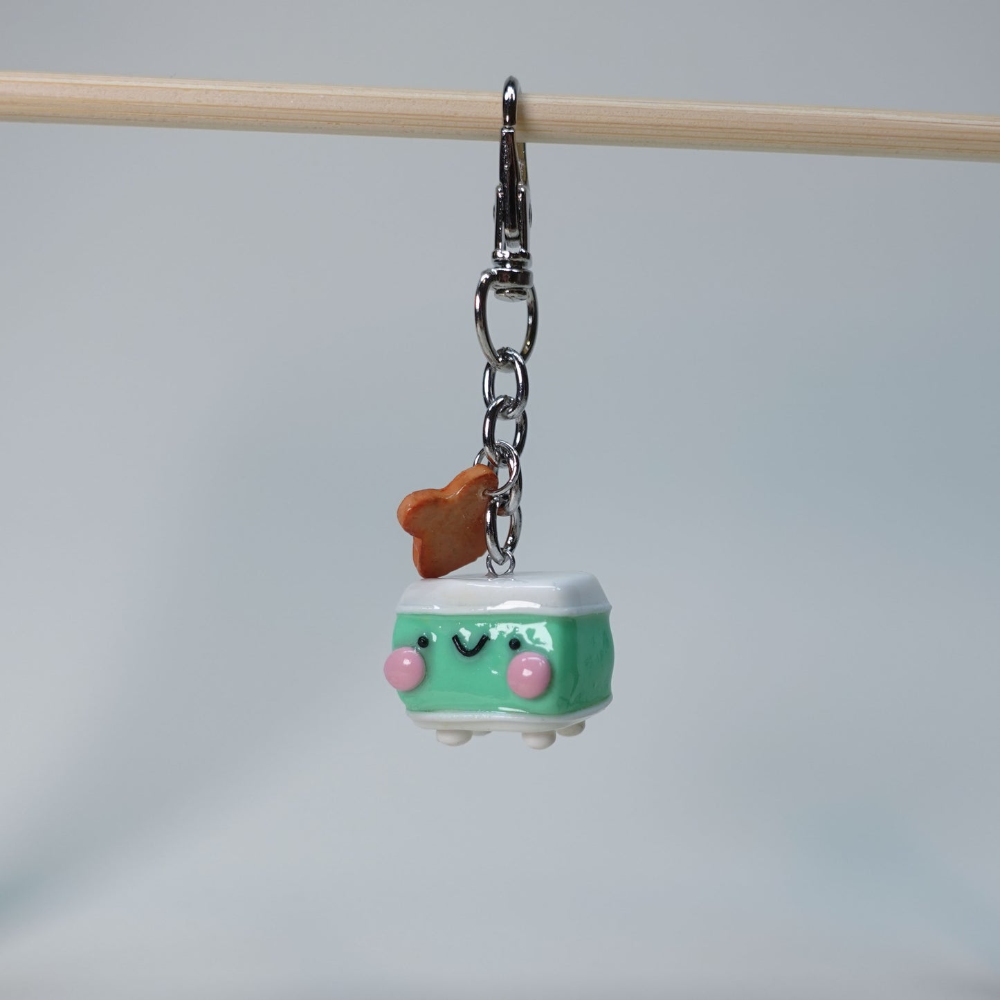 Handmade teal toaster keychain with dangling toast charm featuring red jam detail, playful pastel accessory for keys or bags, limited edition design.