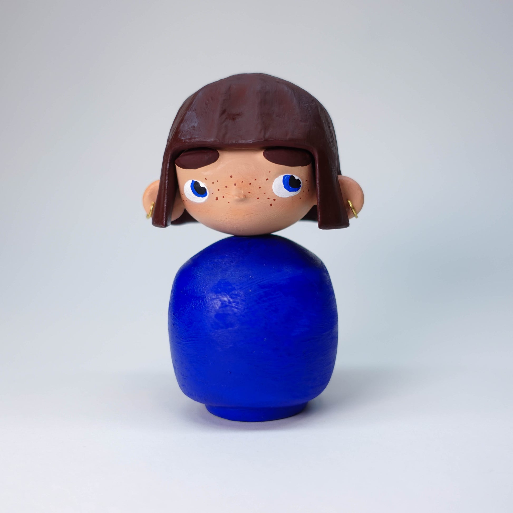 Hand-painted Püpi Bloom sculpture with blue body, brown hair, holding earring, slightly side-eyeing expression, unique collectible art piece, one-of-a-kind.