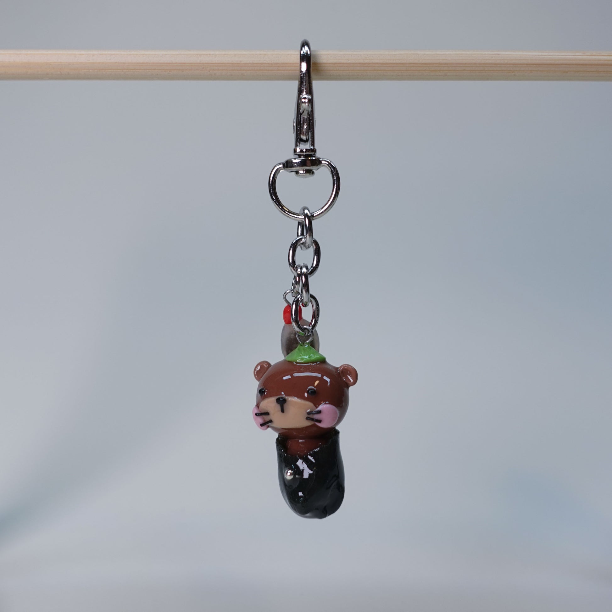 Small handmade otter keychain holding sushi, with dangling soy fish charm, photographed on neutral background, limited edition accessory.