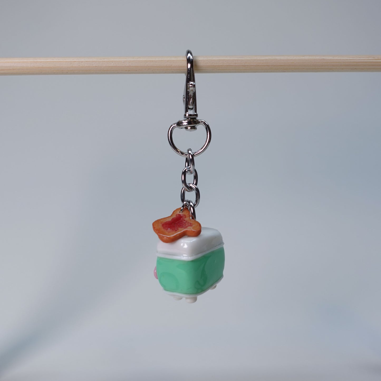 Teal handmade toaster keychain with a small hanging toast charm topped with jam, photographed against a soft neutral background.