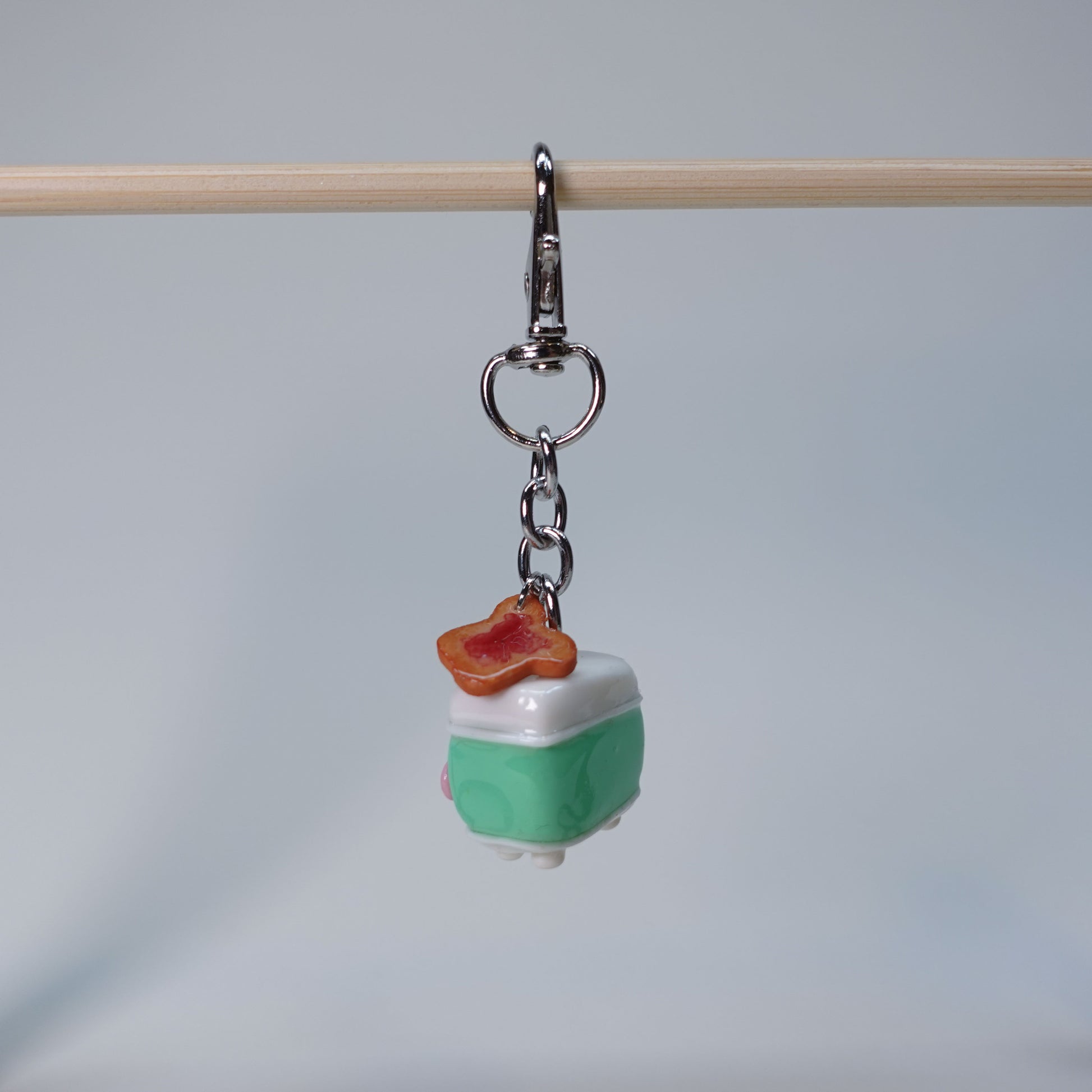 Teal handmade toaster keychain with a small hanging toast charm topped with jam, photographed against a soft neutral background.