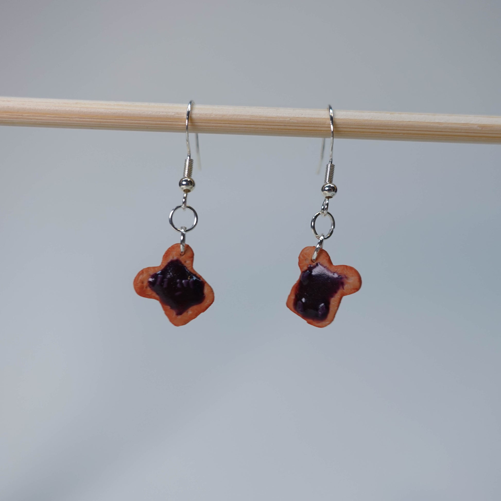 Set of five handmade Toast with Jam earrings, each pair unique with slight burn, blueberry jam, or strawberry jam topping, photographed on neutral background, limited edition.