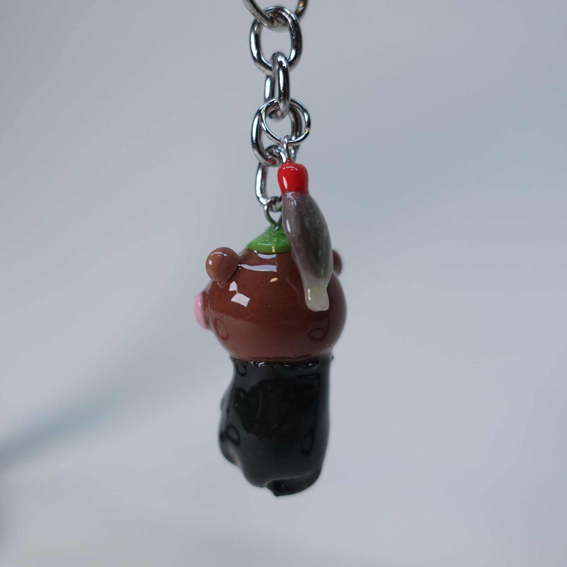 Small handmade otter keychain holding sushi, with dangling soy fish charm, photographed on neutral background, limited edition accessory.