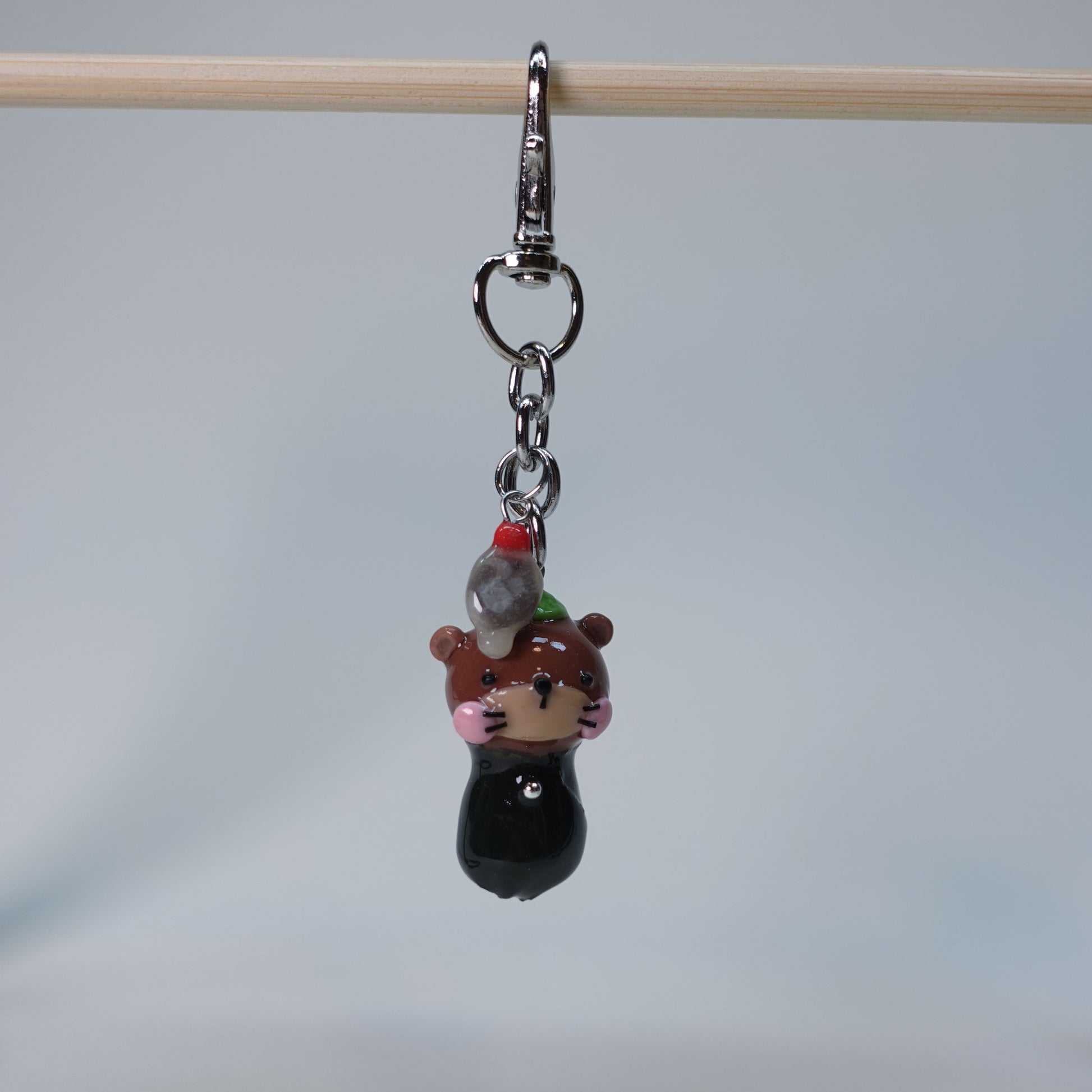 Small handmade otter keychain holding sushi, with dangling soy fish charm, photographed on neutral background, limited edition accessory.