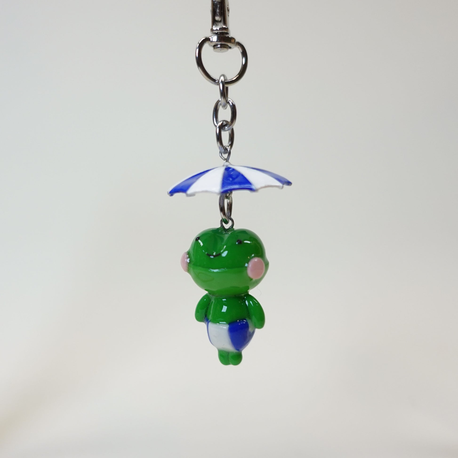 Handmade polymer clay frog keychain wearing a colorful summer umbrella hat with a glossy UV resin finish.