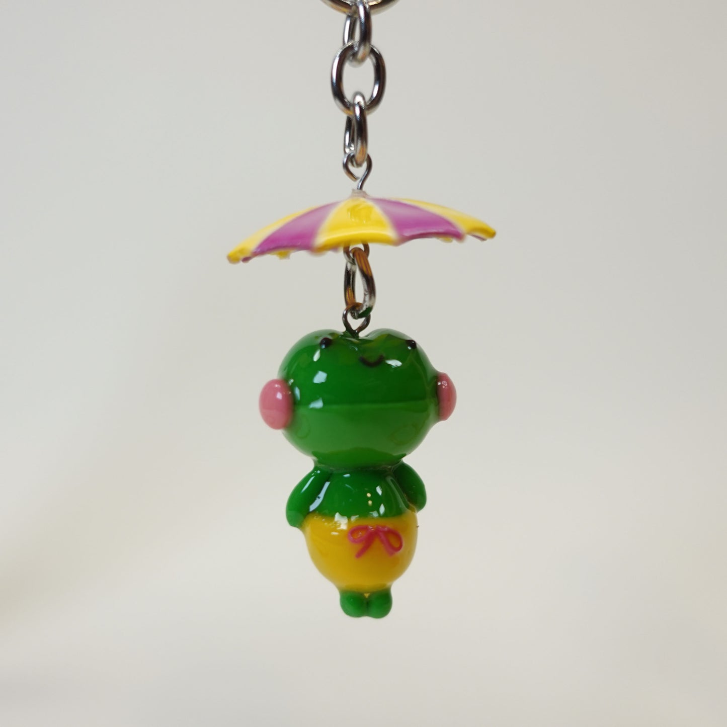 Handmade polymer clay frog keychain wearing a colorful summer umbrella hat with a glossy UV resin finish.