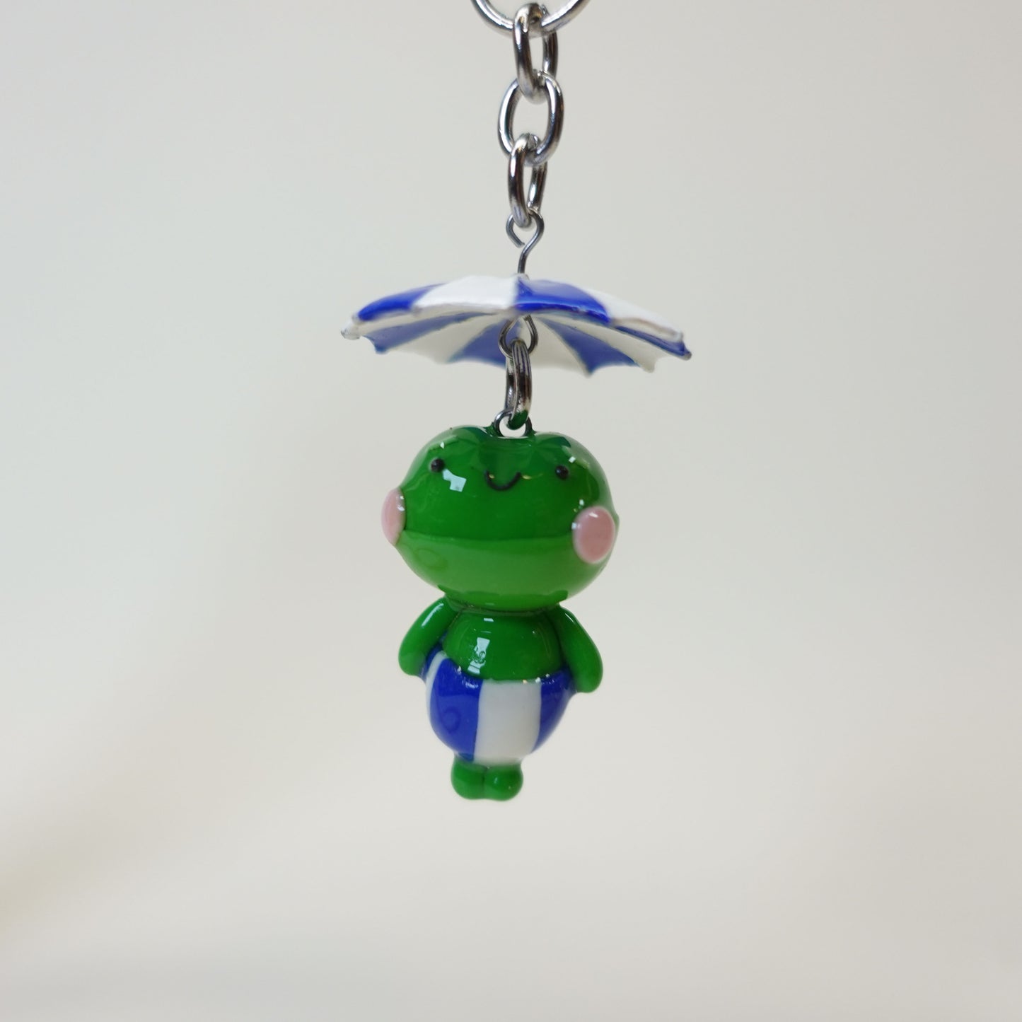 Handmade polymer clay frog keychain wearing a colorful summer umbrella hat with a glossy UV resin finish.