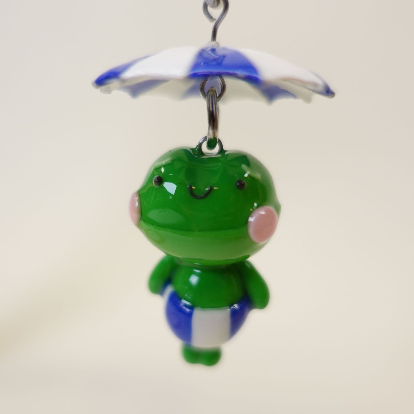 Handmade polymer clay frog keychain wearing a colorful summer umbrella hat with a glossy UV resin finish.
